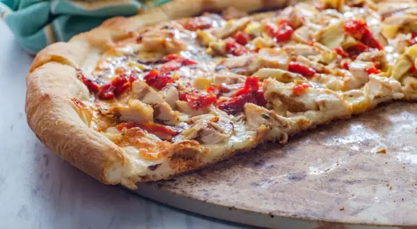 Pyszna pizza włoska z kurczakiem i suszonymi pomidorami, z chrupiącym brzegiem, na kamieniu do pieczenia.