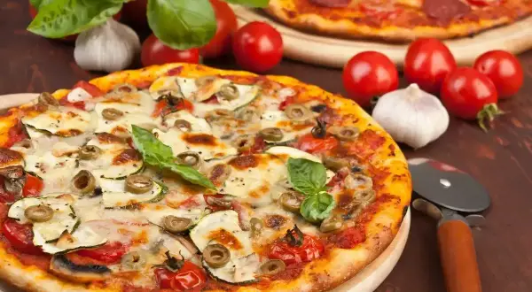 Pyszna pizza z cukinią, oliwkami i pomidorkami, obok surowe pieczarki na pizze, czosnek i bazylia.