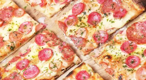 Kawałki pizzy z kiełbasą i serem, posypane ziołami. Idealne ciasto na pizzę dla każdego smakosza.