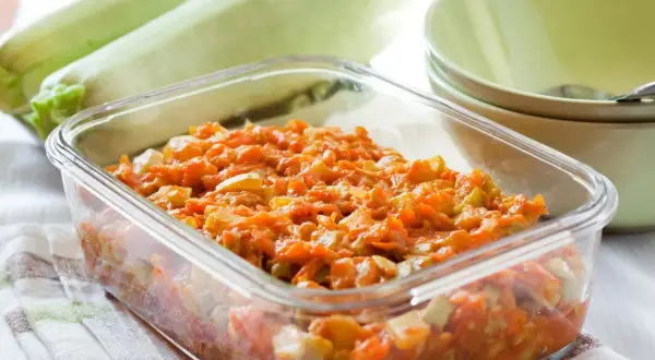 Pyszny bigos z cukinii w szklanym naczyniu, obok świeże cukinie i miseczki.