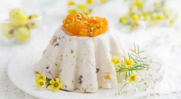 Tradycyjna pascha wielkanocna, udekorowana kandyzowanymi owocami i pistacjami, otoczona wiosennymi kwiatami.