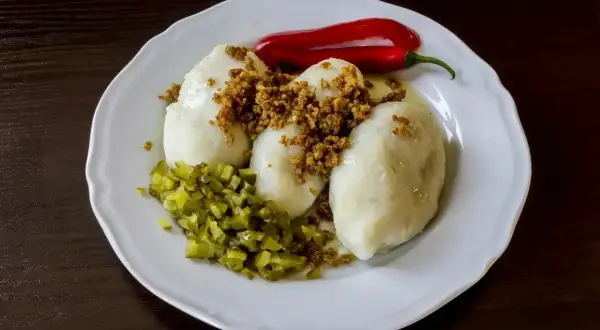 Gotowe kartacze na talerzu, posypane skwarkami, z ogórkiem kiszonym i papryczką chili. Idealne do podania według przepisu na kartacze.