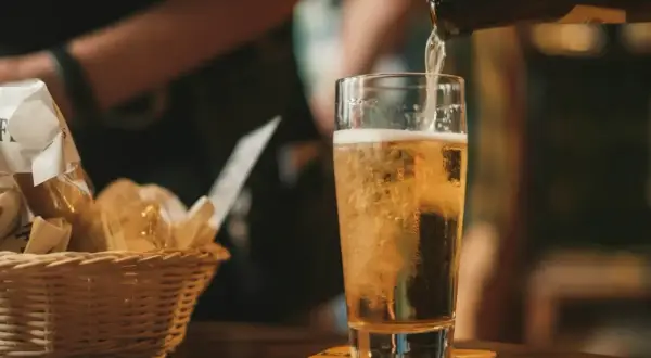 Złociste piwo IPA i APA leje się do szklanki. Obok koszyk z przekąskami.