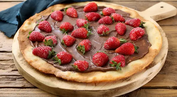 Słodka pizza z truskawkami i kremem czekoladowym na drewnianej desce. Idealna na deser!
