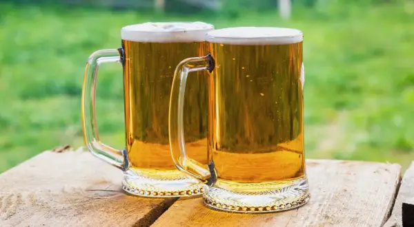 Dwa kufle złocistego piwa z pianką, gotowe do degustacji. Idealne na lato, przypominają o tym, jak zrobić piwo w domowym zaciszu.