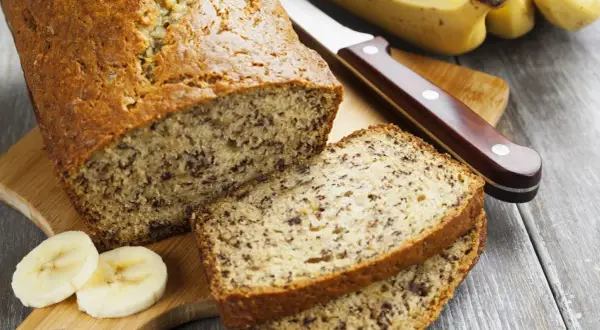 Pyszny chlebek bananowy, pokrojony na kromki, z bananami i nożem na desce.