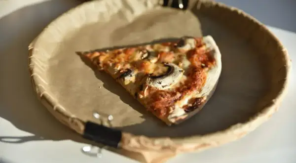 Kawałek pizzy z pieczarkami na papierowym talerzu. Zastanawiasz się nad ciasto na pizze kcal?