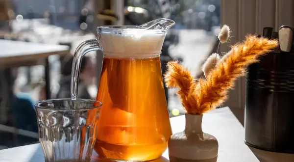 Dzbanek orzeźwiającego helles bier z pianką obok szklanki i ozdobnej trawy.
