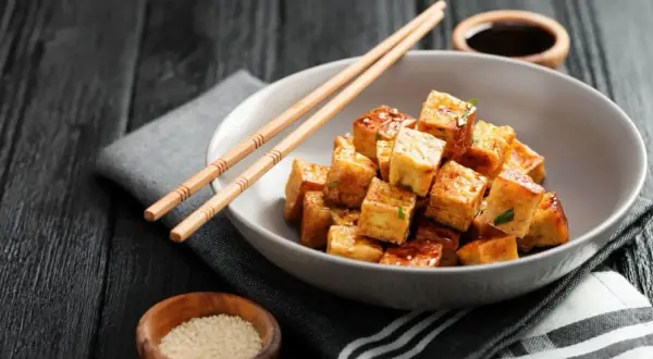 Kostki smażonego tofu, z którego jest tofu, w sosie, pałeczki, sezam i sos sojowy na ciemnym tle.