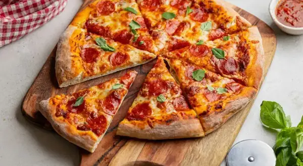 Pyszna pizza pepperoni, idealna na ostro, z ciągnącym się serem i świeżą bazylią, podana na drewnianej desce.
