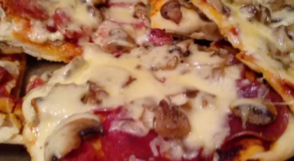 Pyszna domowa pizza z pieczarkami i salami, obficie posypana ciągnącym się serem. Idealna na wieczór z bliskimi.