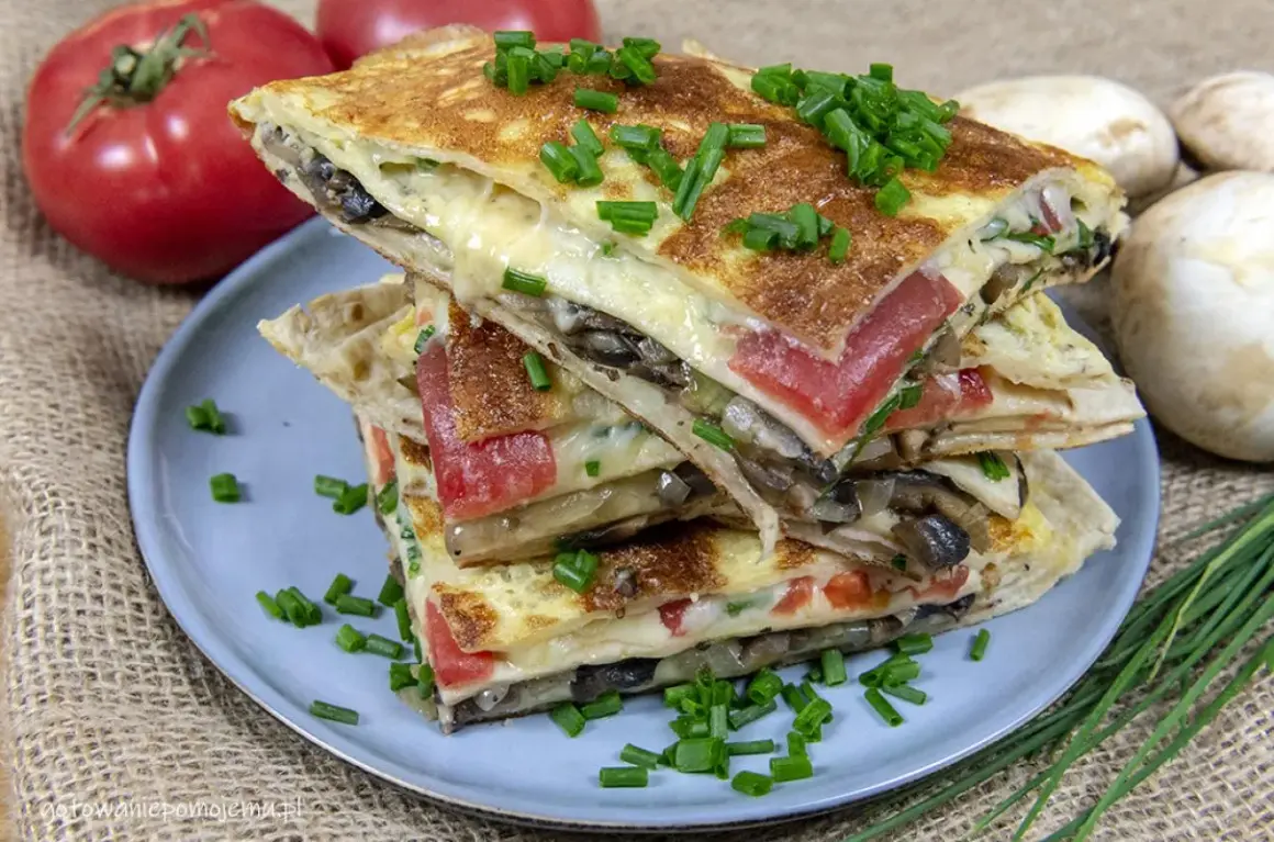 Pyszna tortilla na śniadanie z serem, pomidorami i grzybami, posypana szczypiorkiem.