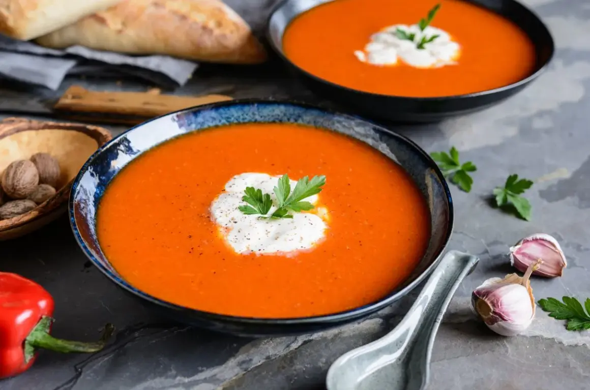 Aksamitny zupa krem z papryki, udekorowana śmietaną i natką pietruszki, podana z pieczywem i czosnkiem.