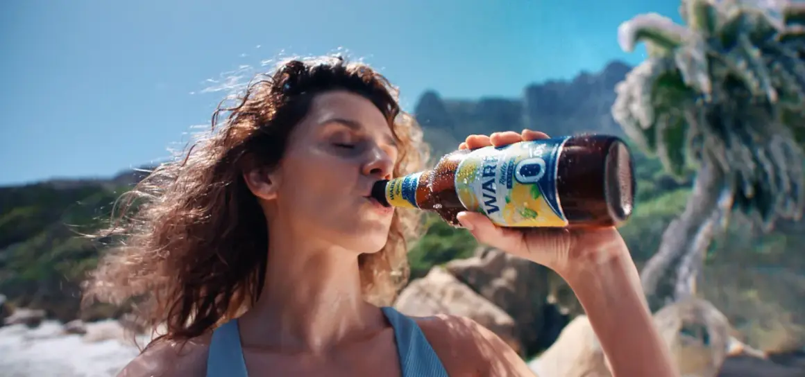 Kobieta pije piwo Zlatý Bažant 0,0% na plaży.