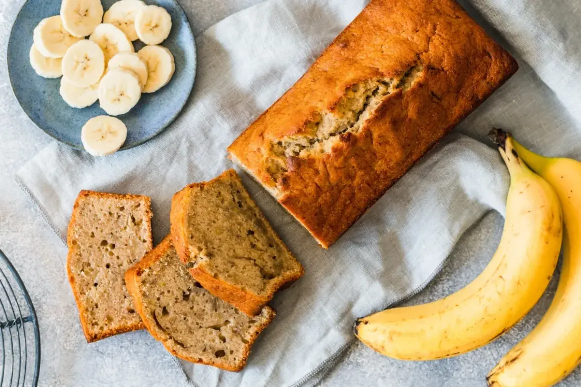 Pyszny chlebek bananowy z dwóch bananów, pokrojony na kromki. Obok leżą świeże banany i talerzyk z plasterkami.