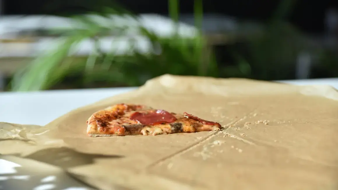Kawałek pizzy z salami na śniadanie, leżący na papierze do pieczenia.
