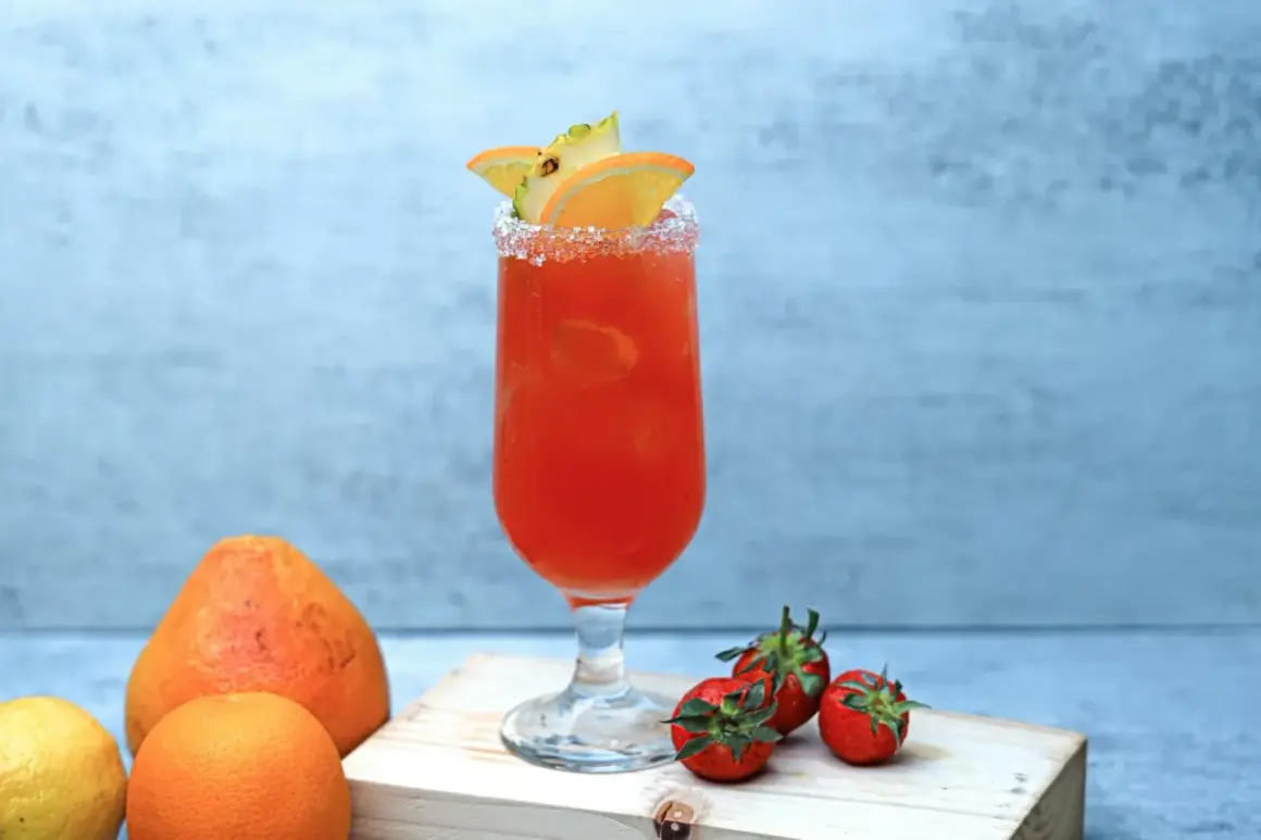 Orzeźwiający drink z pomarańczy i ananasa, z solą na brzegu kieliszka. Obok leżą truskawki, cytryna i pomarańcza. Idealny na lato, jak piwo cytrynowe.