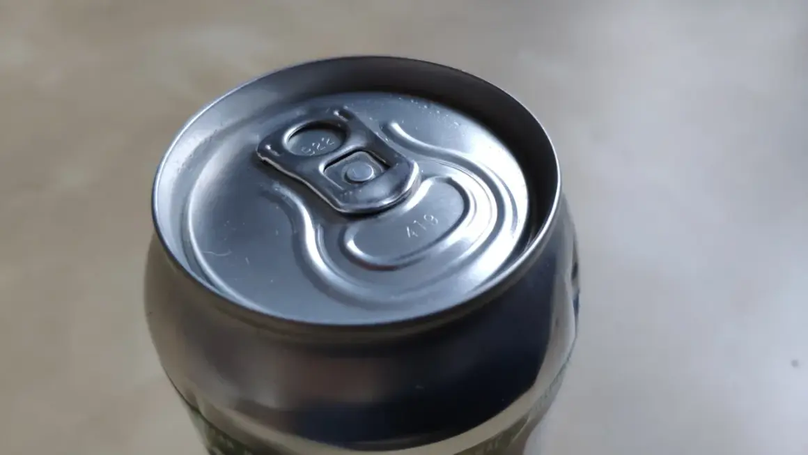 Metalowa puszka piwa z widocznymi kropkami na wieczku, które mogą oznaczać datę produkcji lub numer partii.