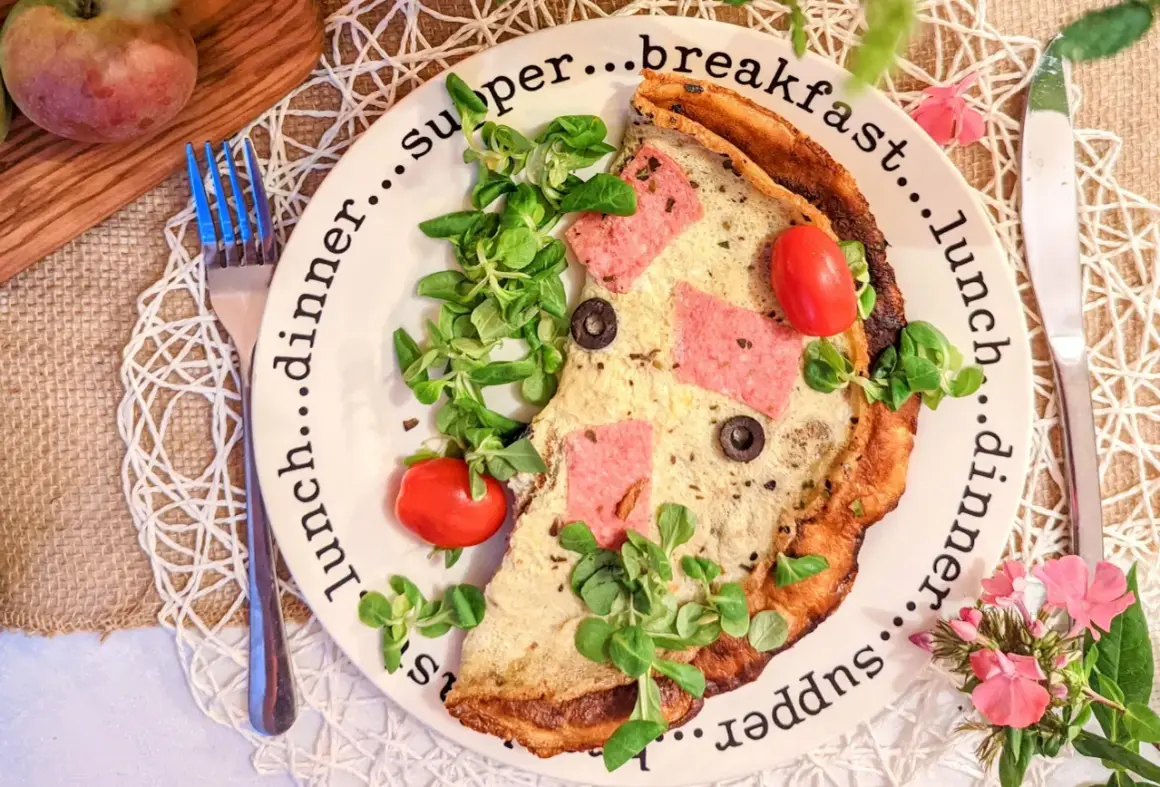 Pyszne, sycące śniadanie do pracy: omlet z szynką, pomidorkami i oliwkami, udekorowany świeżą sałatką.