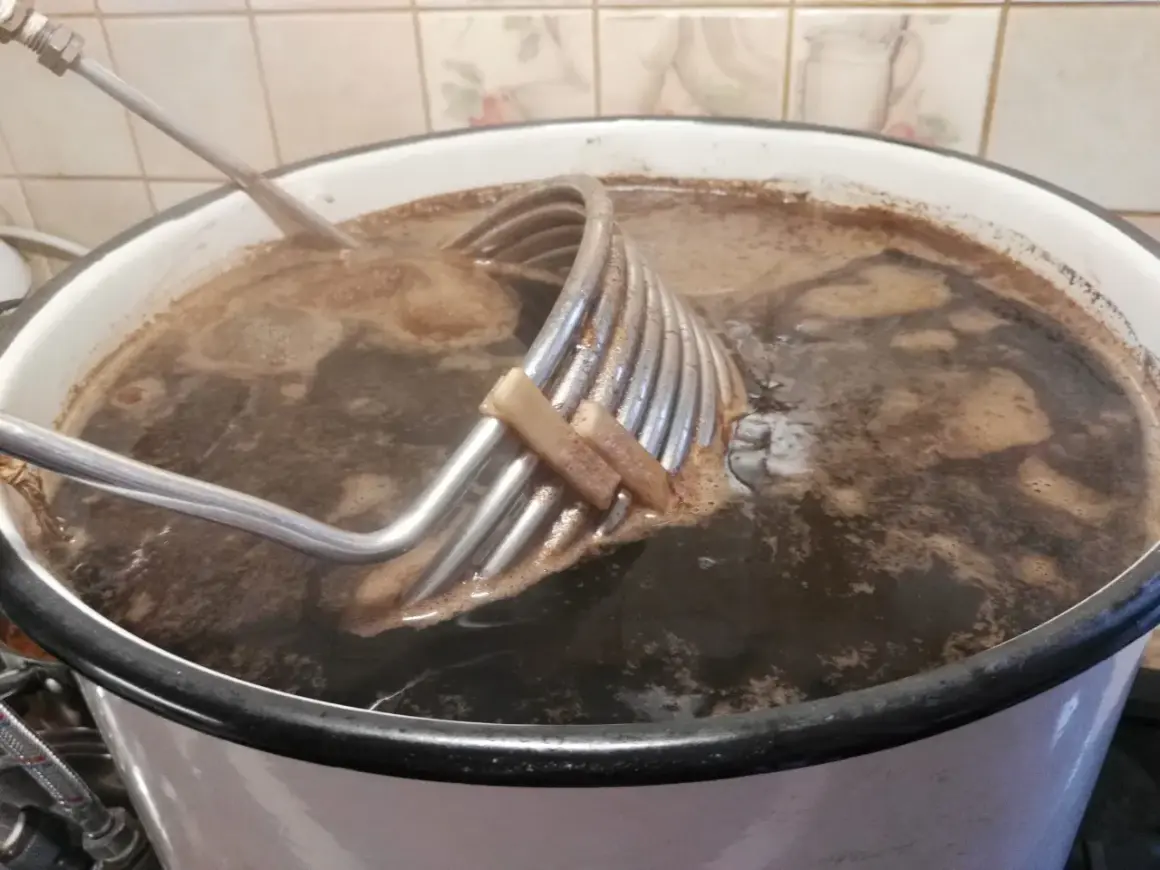 Gotowanie brzeczki do imperial stout. Metalowa chłodnica zanurzona w ciemnym płynie.