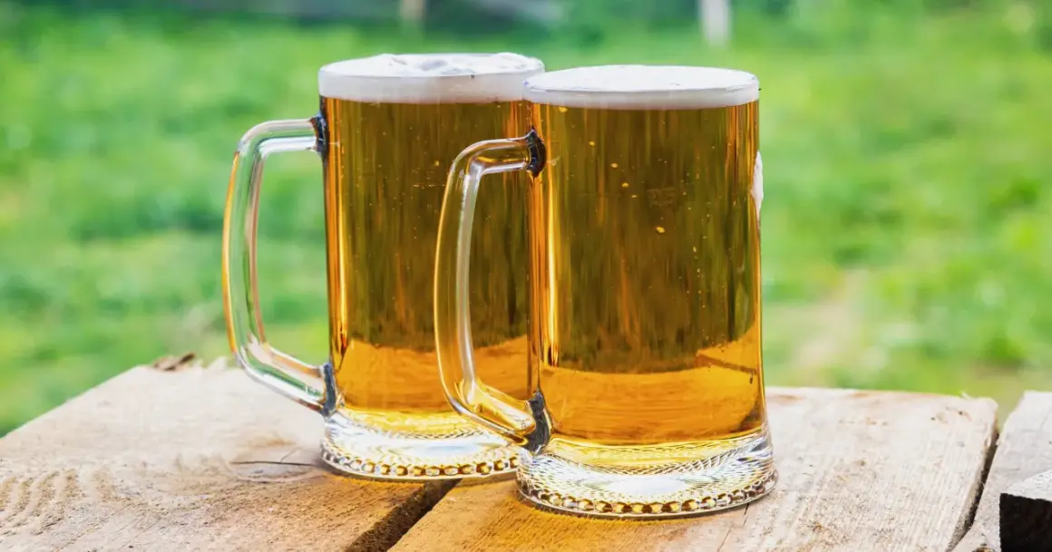 Dwa kufle złocistego piwa z pianką, gotowe do degustacji. Idealne na lato, przypominają o tym, jak zrobić piwo w domowym zaciszu.