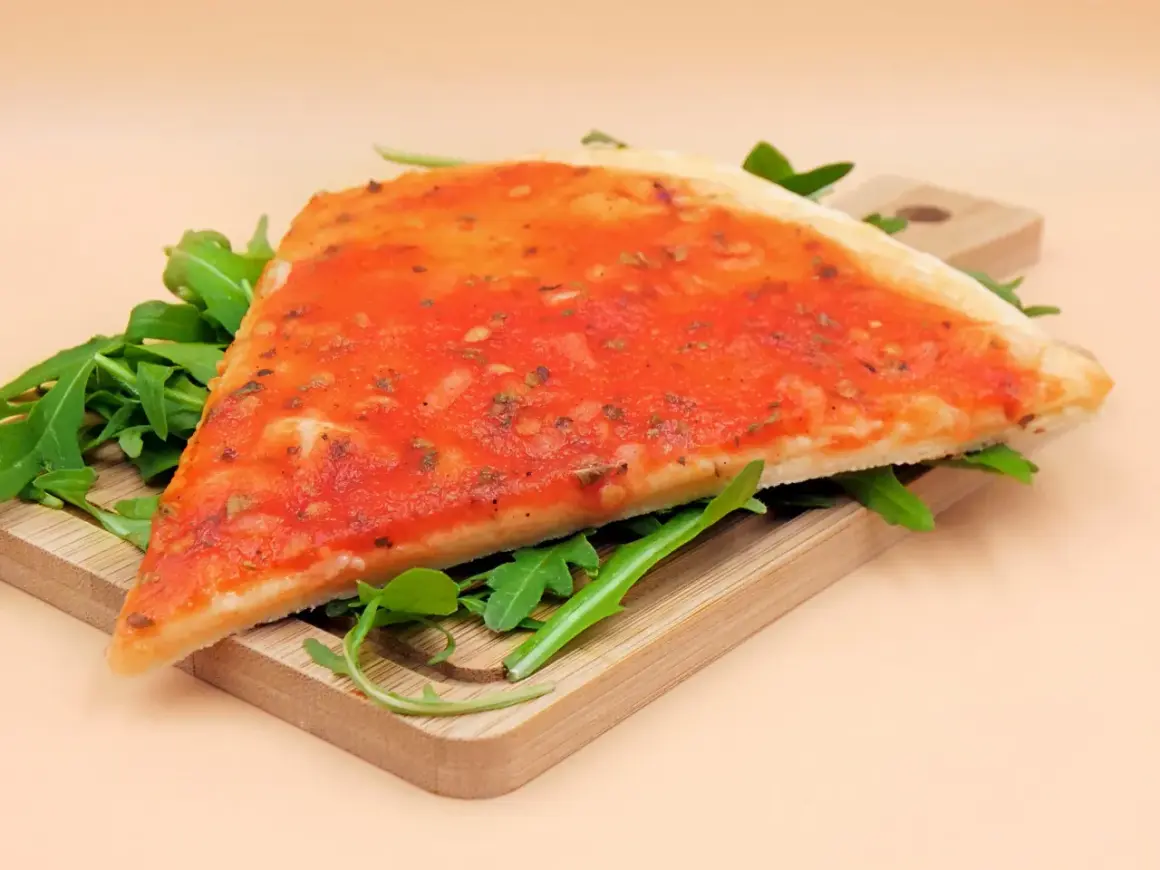 Kawałek pizzy marinara na desce z rukolą. Zastanawiasz się nad pizza marinara kcal?