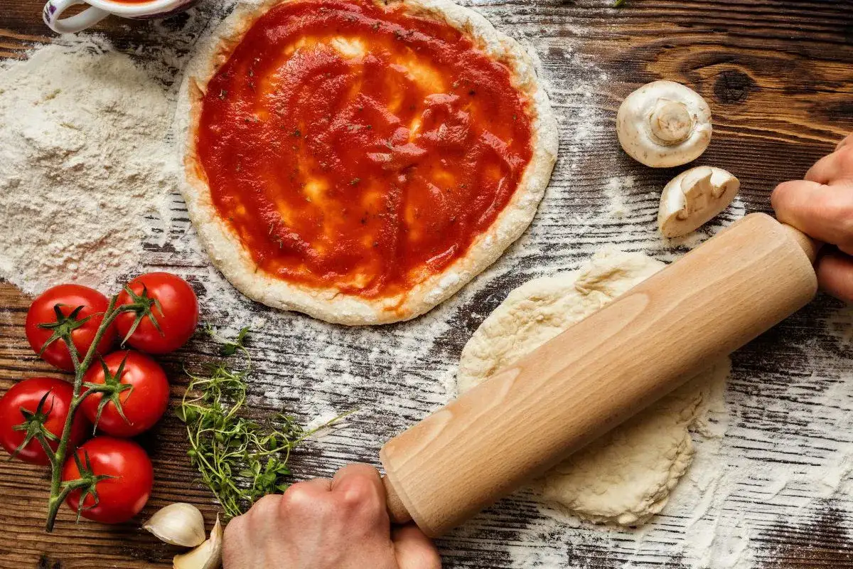 Przygotowania do domowej pizzy: ciasto, pomidory, czosnek, zioła i pyszny sos do pizzy.