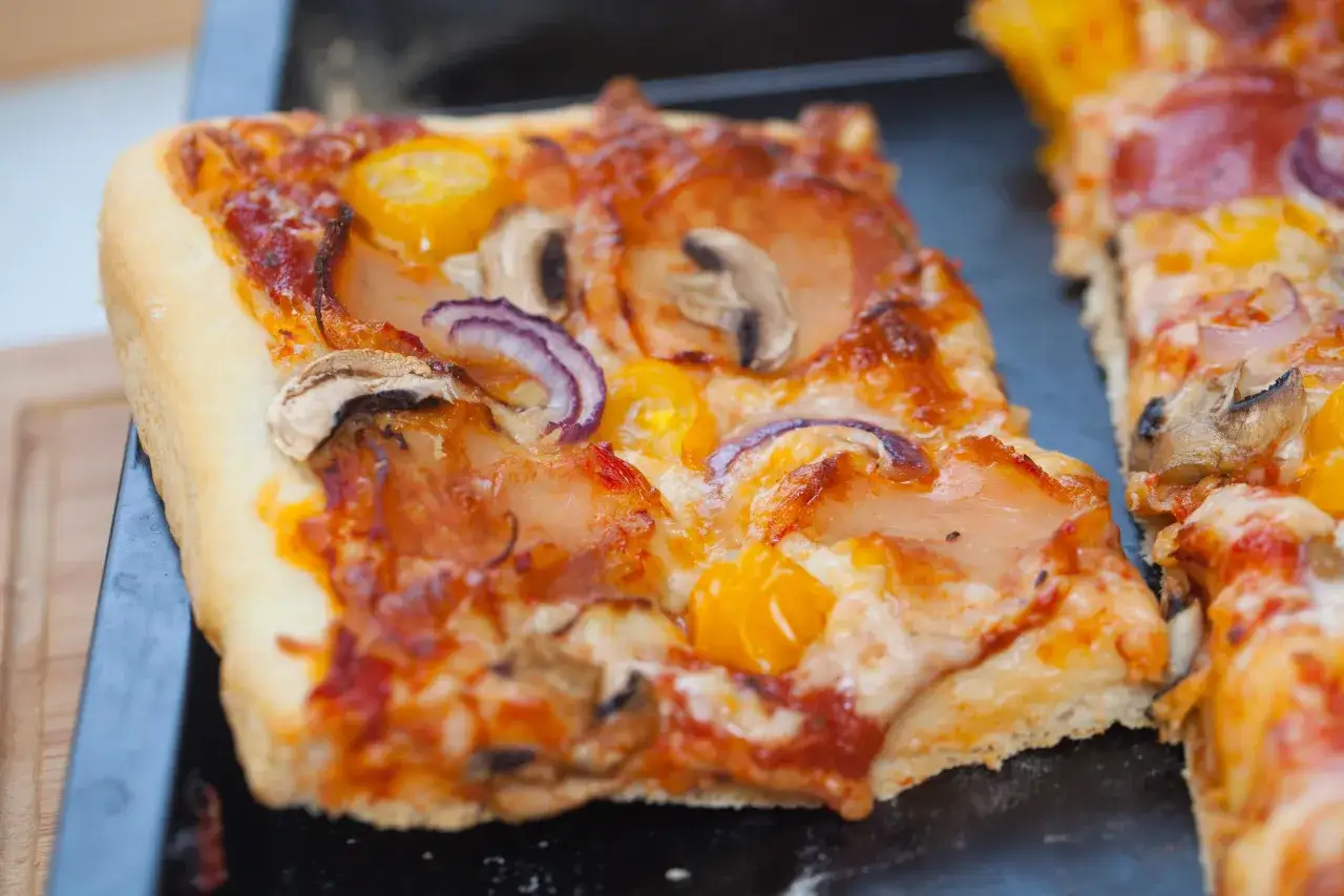 Pyszne ciasto na pizzę amerykańską z pieczarkami, cebulą i żółtymi pomidorkami, prosto z pieca.