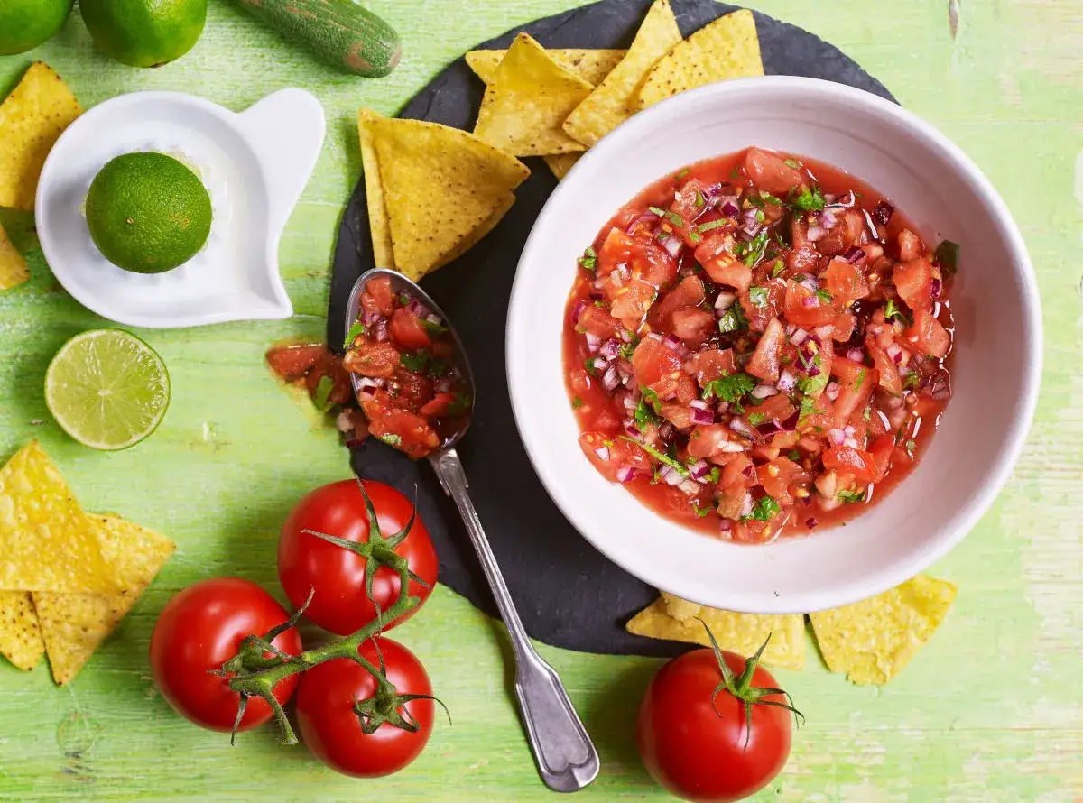 Świeża salsa pomidorowa z cebulą i kolendrą, podana z nachos i limonką. Idealna na przekąskę.