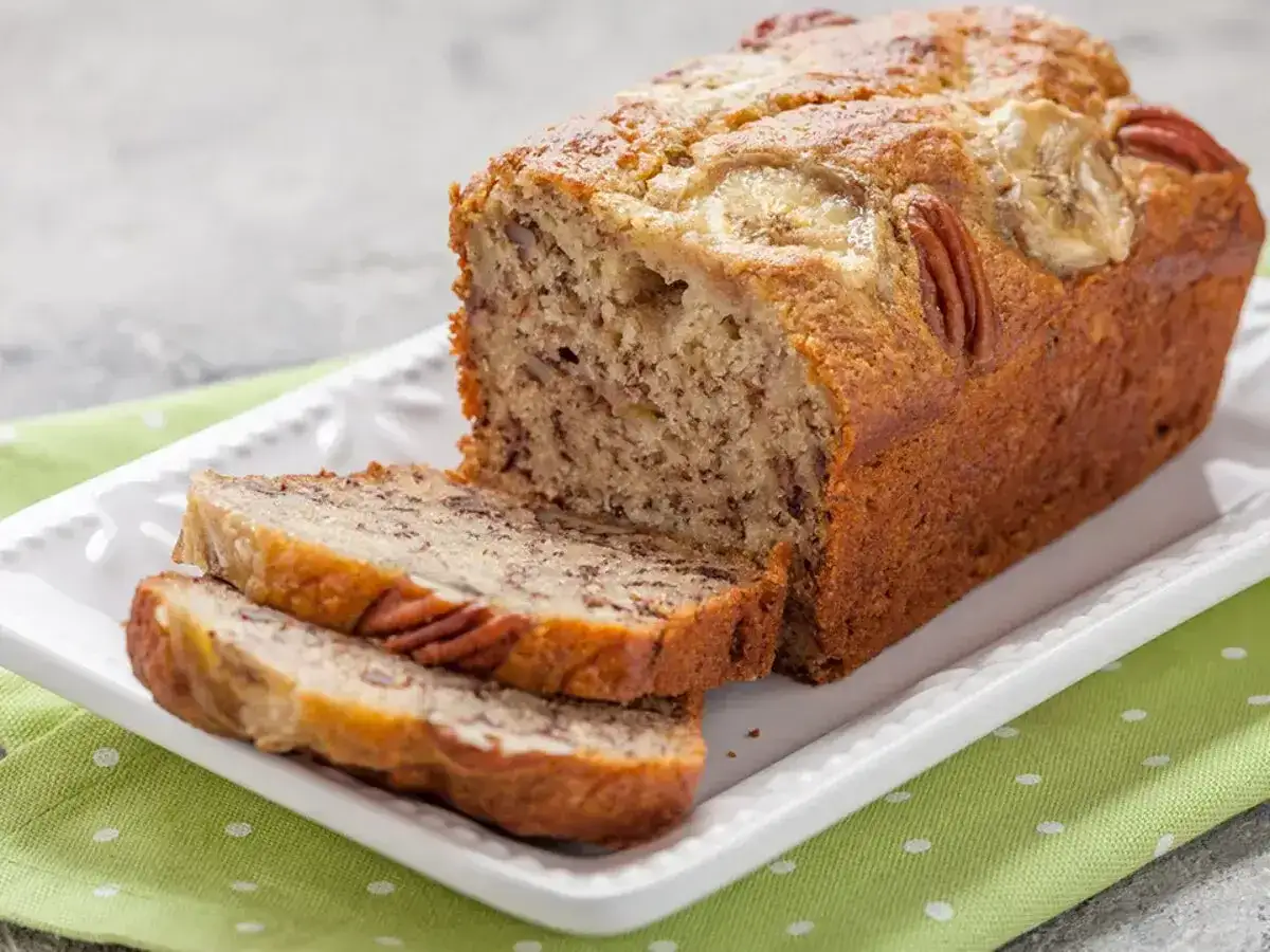 Pyszny chlebek bananowy z dwóch bananów, z kawałkami orzechów pekan i plasterkami banana na wierzchu. Idealny na podwieczorek.