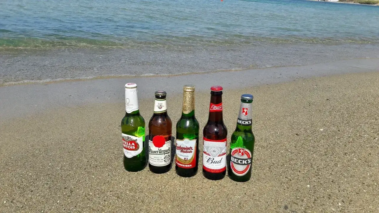 Pięć butelek piwa na plaży, z morzem w tle. Idealne na upalny dzień nad morzem.