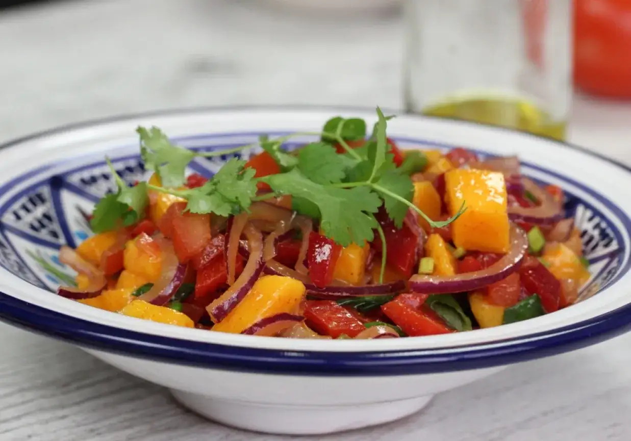 Kolorowa salsa mango z pomidorami, papryką i czerwoną cebulą, udekorowana świeżą kolendrą.