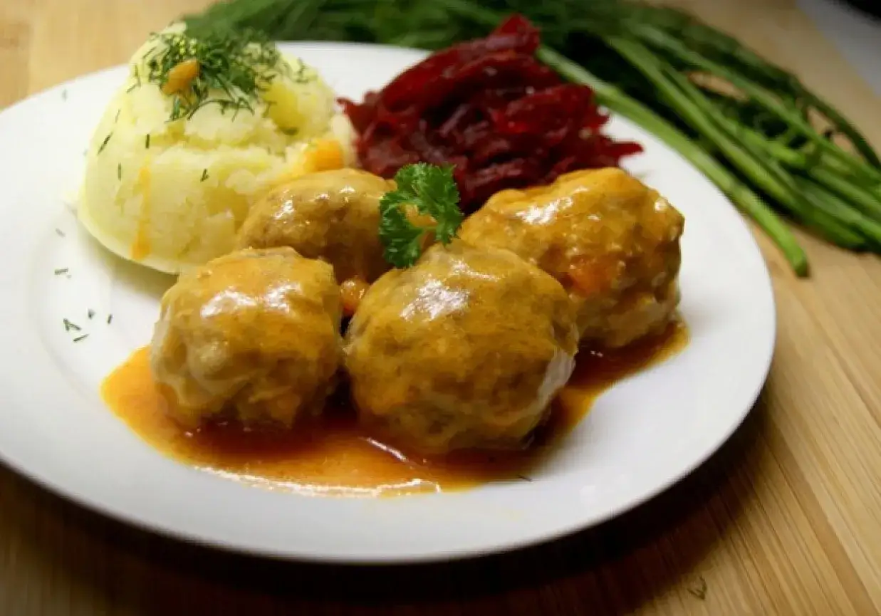Pulpety w sosie pomidorowym, podane z purée ziemniaczanym i buraczkami. Danie ozdobione natką pietruszki.