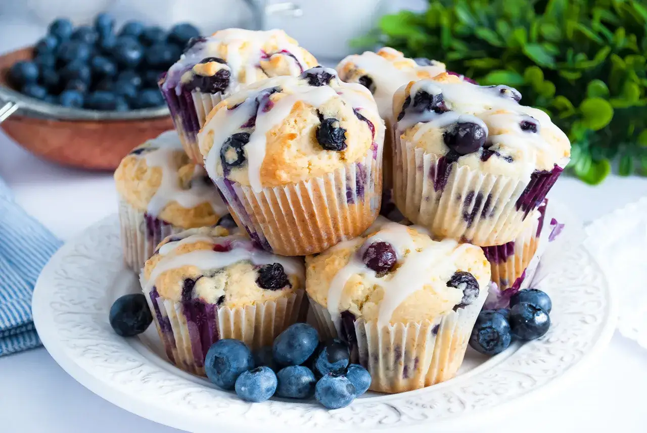 Stos pysznych muffinek jogurtowych z lukrem i borówkami, ozdobione świeżymi owocami.