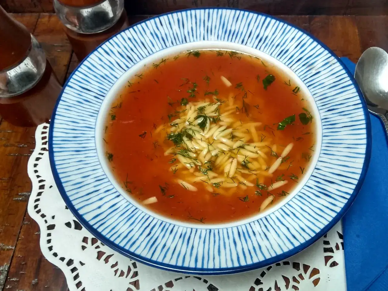 Aksamitna zupa pomidorowa na bulionie warzywnym, z makaronem orzo i świeżym koperkiem, podana na talerzu z niebieskimi paskami.