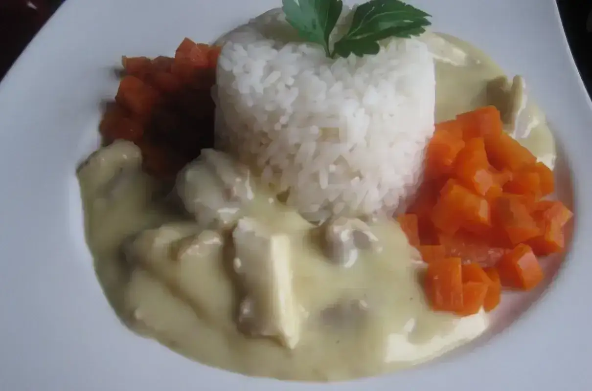 Ryż z kawałkami kurczaka w kremowym sosie do potrawki, podany z marchewką.
