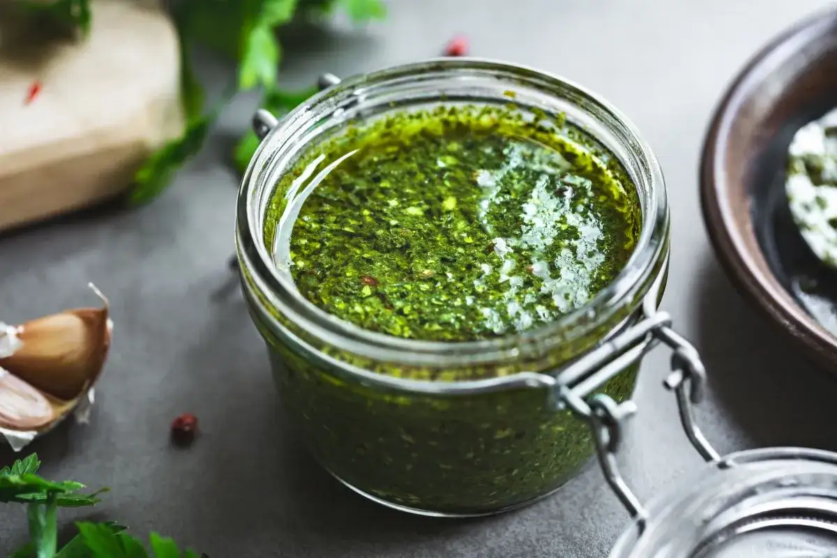 Słoik domowego pesto z bazylii, obok czosnek i świeże zioła. Idealne do makaronu!