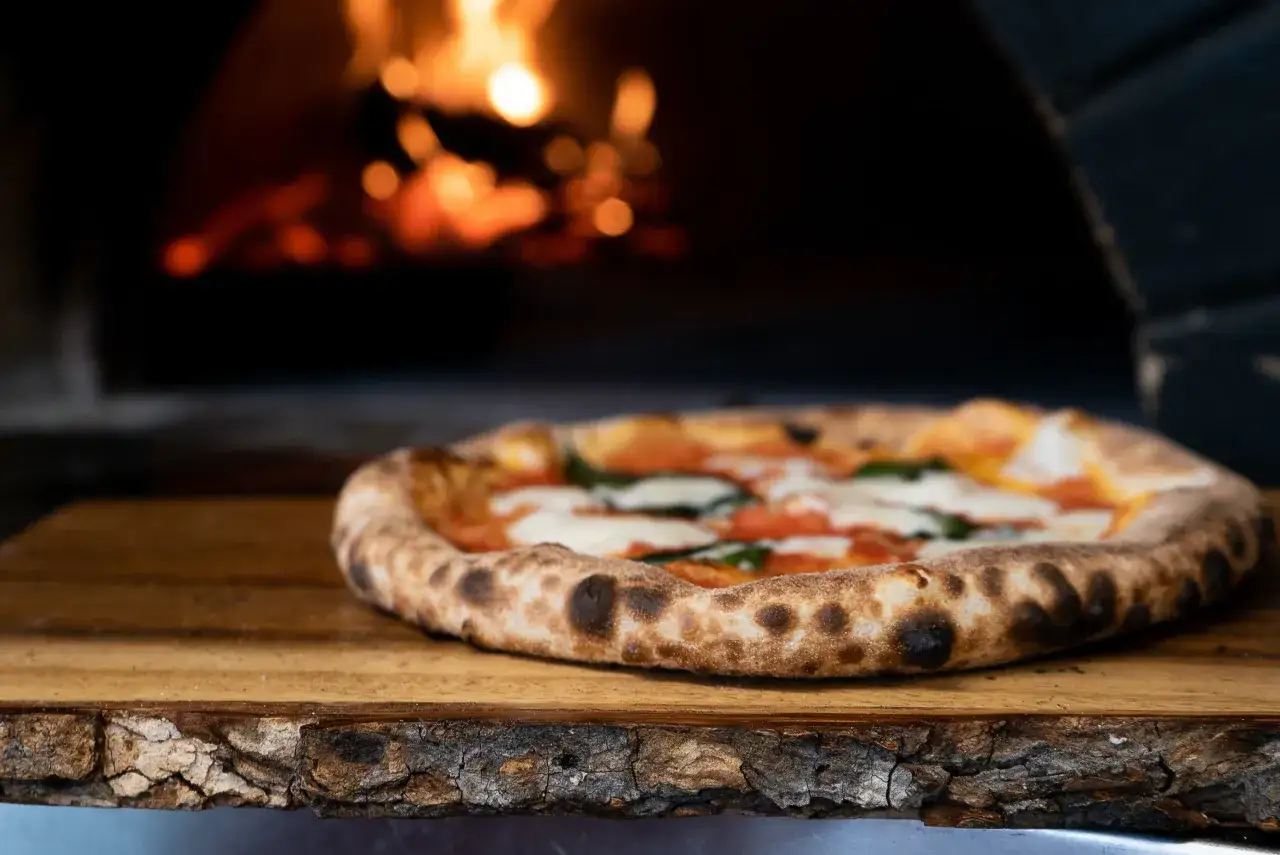 Gorąca pizza na drewnianej desce, w tle płomienie pieca. Czy wiesz, że ciekawostki o pizzy są równie fascynujące, co jej smak?