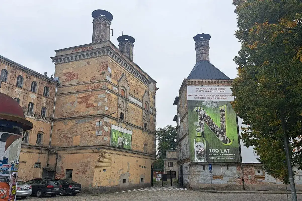 Stare budynki browaru w Namysłowie, z charakterystycznymi kominami i wielką reklamą piwa.