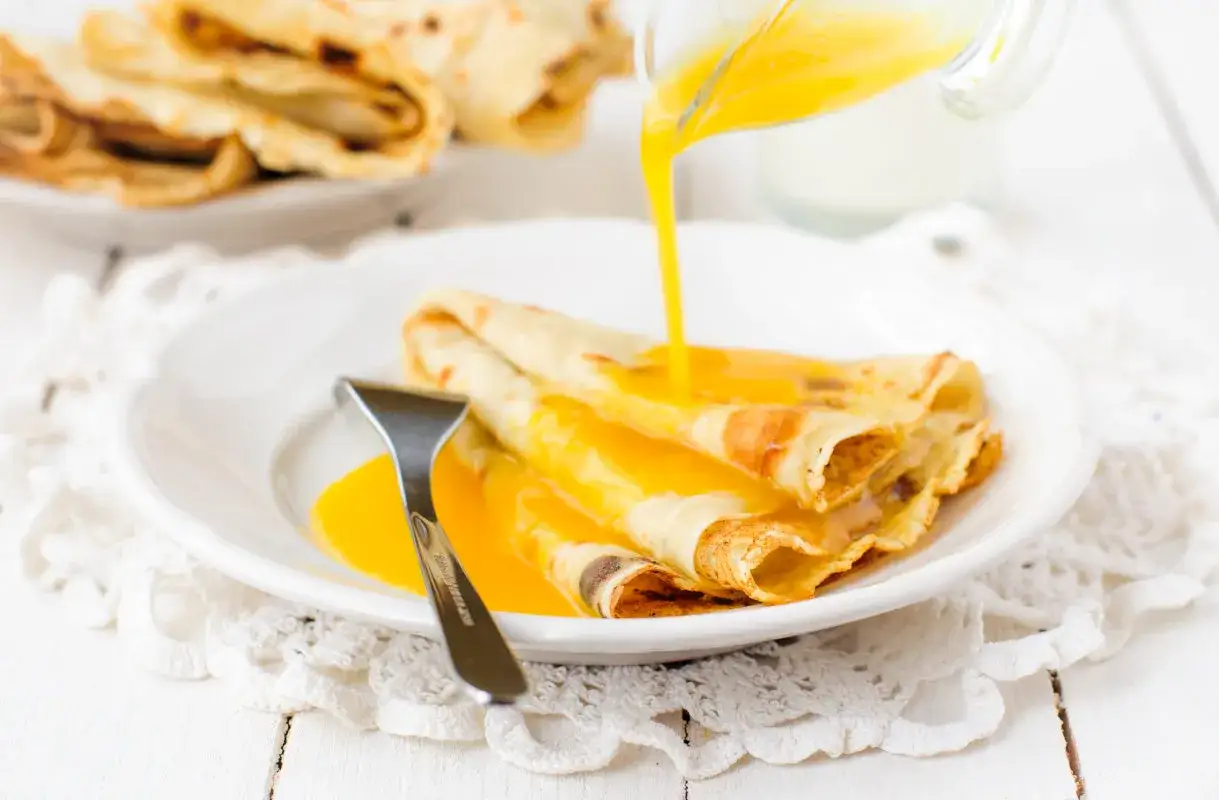Pyszne naleśniki crepes suzette polane gorącym, pomarańczowym sosem. Widelec czeka, by zacząć ucztę.