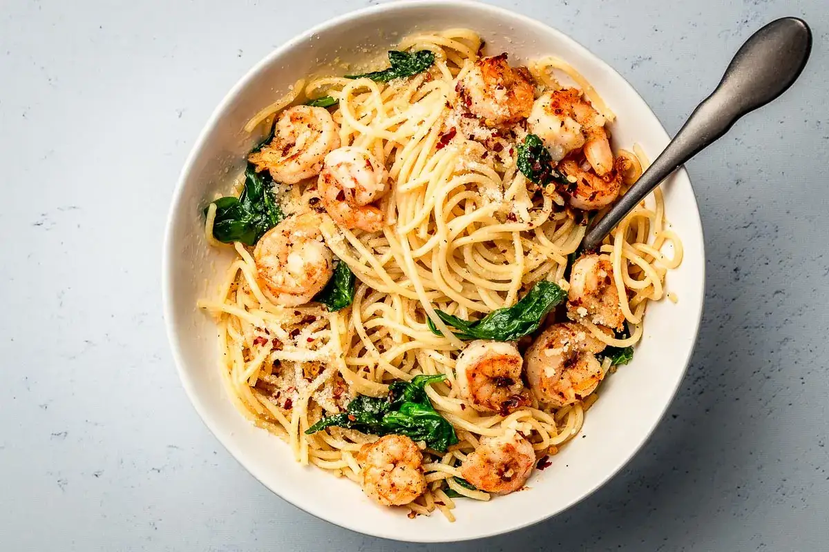 Pyszny przepis z krewetkami: spaghetti z soczystymi krewetkami, szpinakiem i parmezanem, posypane płatkami chili.