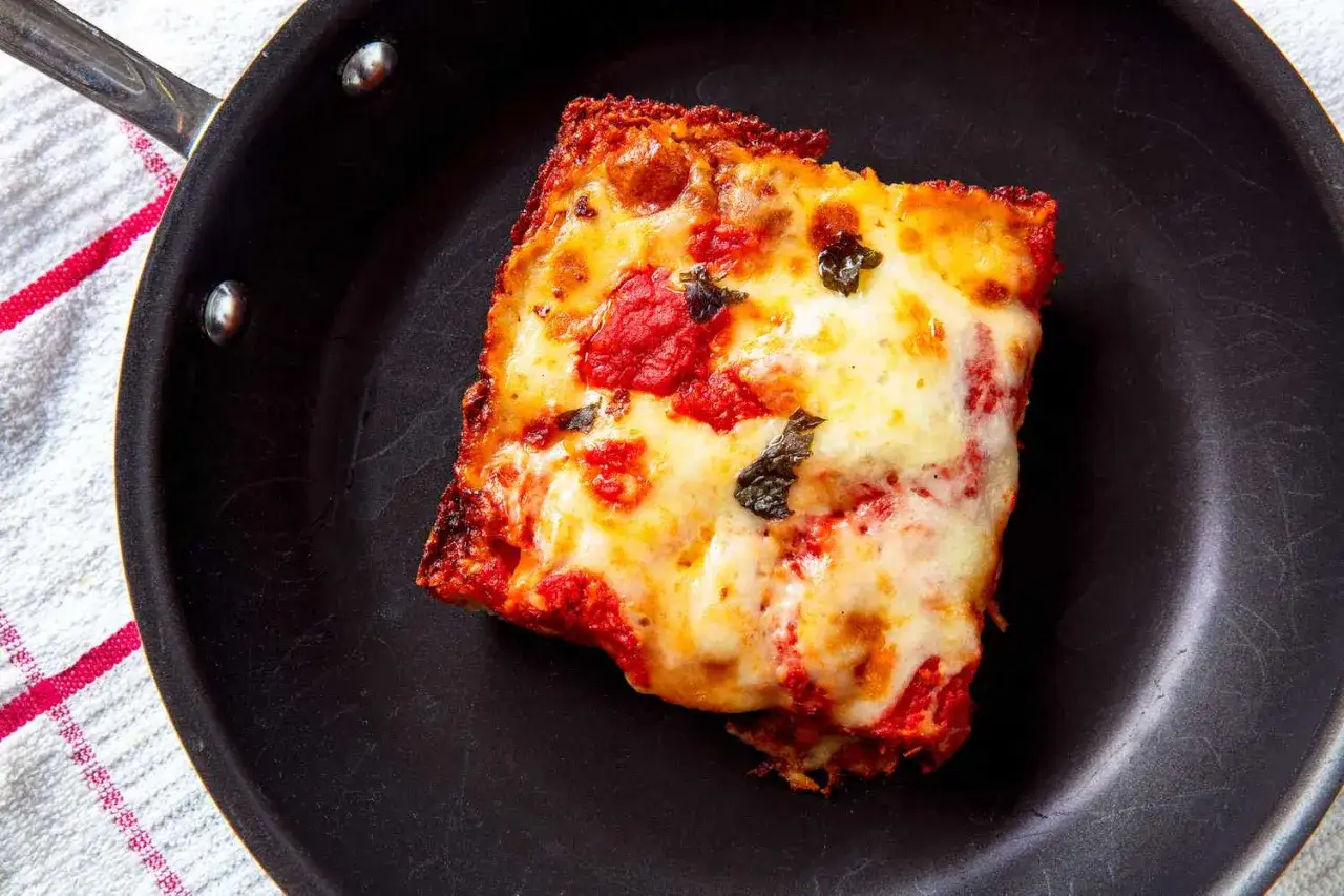 Kawałek pizzy z ciągnącym serem i sosem pomidorowym w czarnej patelni. Idealny sposób, jak odgrzać pizzę na patelni, by była chrupiąca.