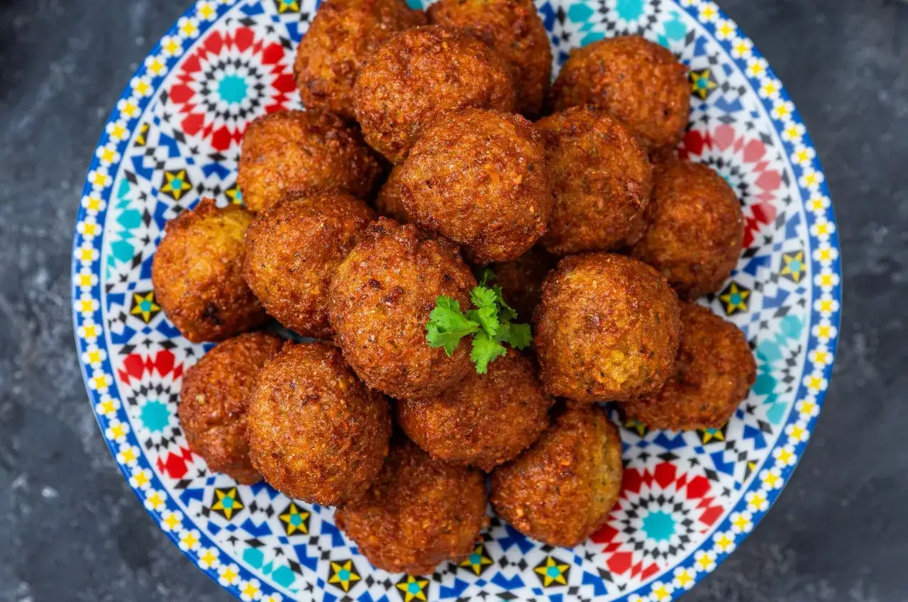 Złociste kulki falafela, idealne do domowego falafel przepis, ułożone na kolorowym talerzu z orientalnym wzorem.