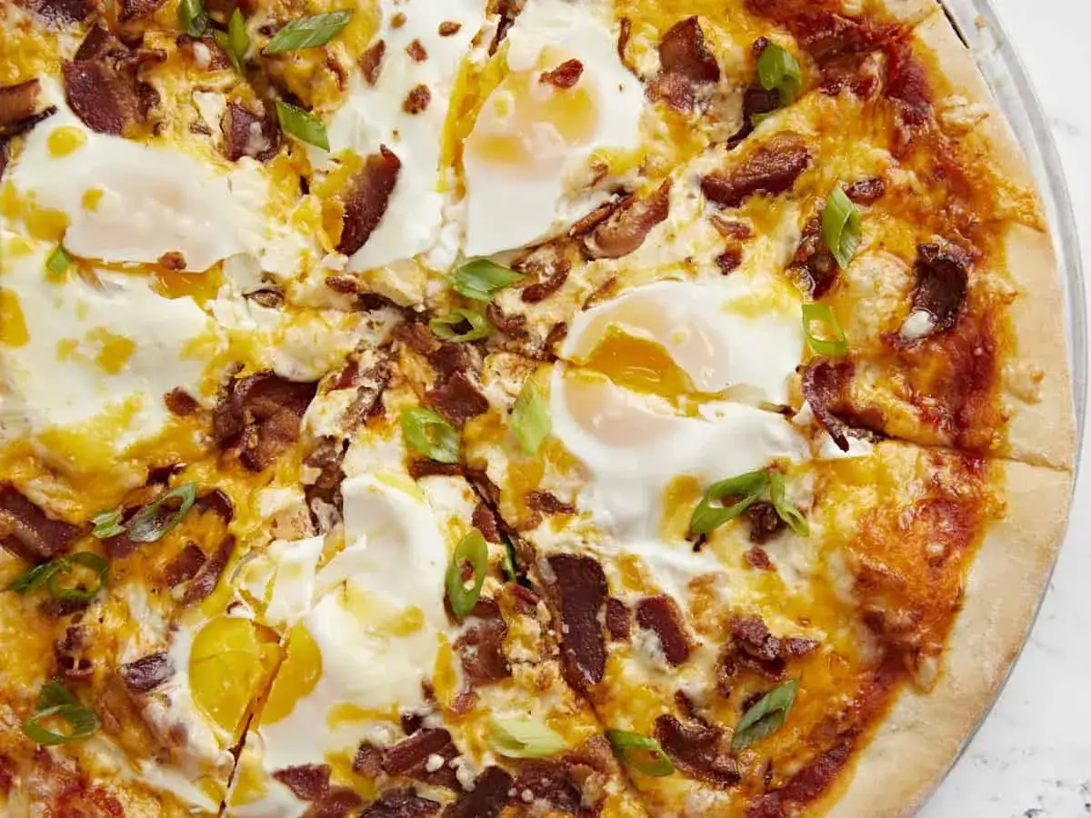 Pyszna pizza na śniadanie z jajkami sadzonymi, chrupiącym boczkiem i zieloną cebulką. Idealny początek dnia!