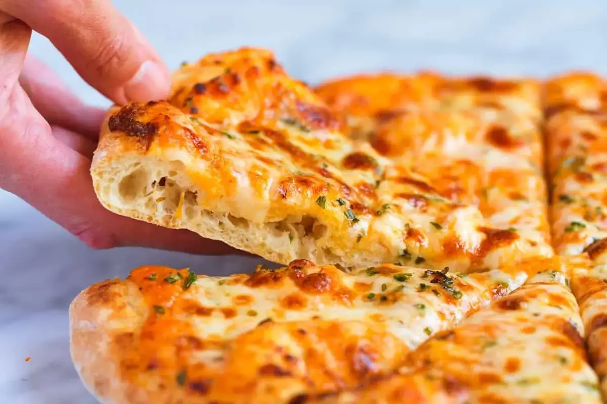 Ręka podnosi kawałek grubej pizzy z ciągnącym się serem i ziołami. Idealna na wieczór filmowy!