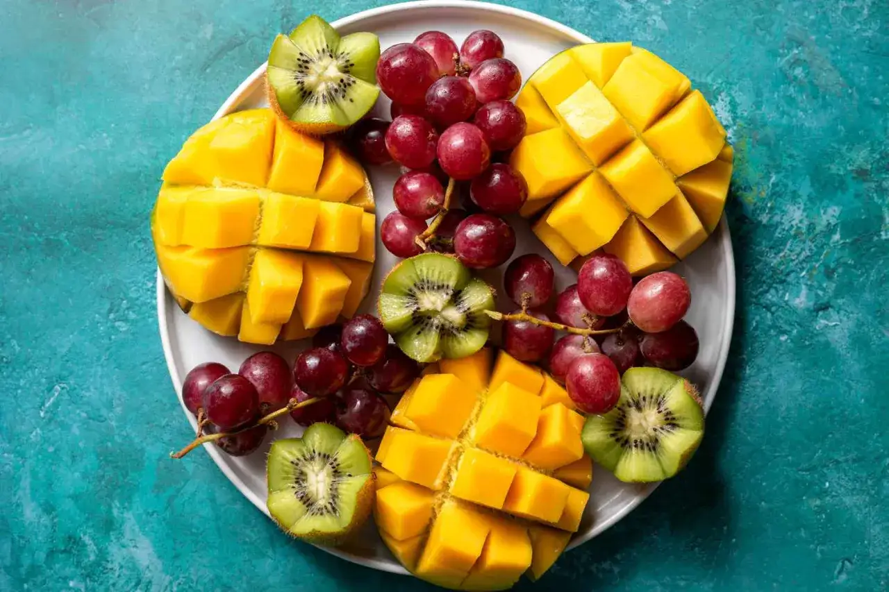 Talerz z pokrojonym mango, winogronami i kiwi. Idealna inspiracja, co zrobić z mango na orzeźwiającą przekąskę.