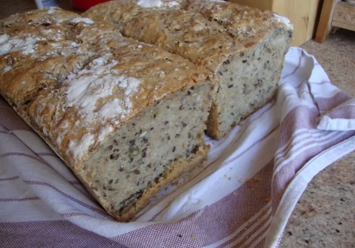 Dwa bochenki chleba na zakwasie, z widocznymi ziarnami, leżą na ręczniku w paski.