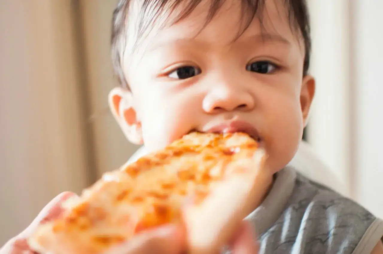 Małe dziecko z radością gryzie kawałek pizzy dla niemowlaka.