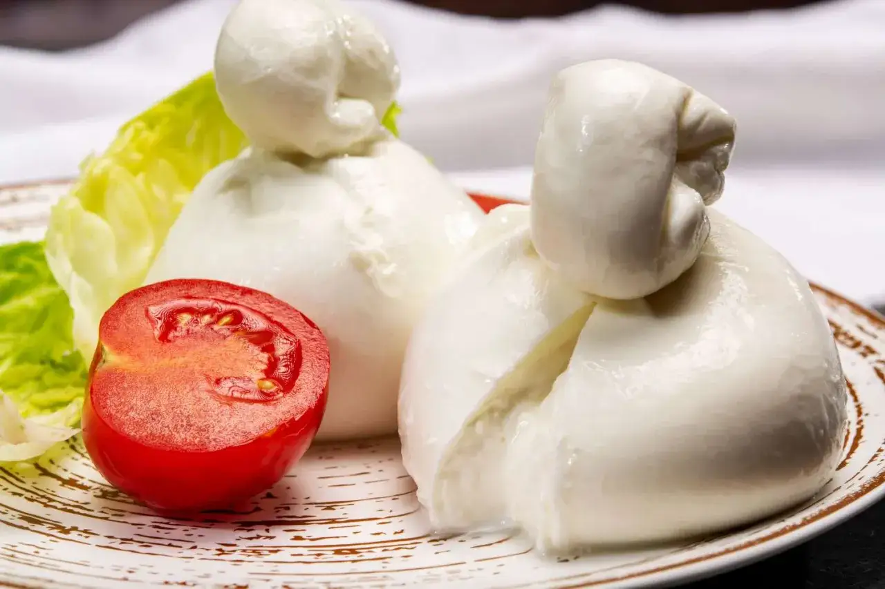 Dwa pękate rodzaje mozzarelli, pomidor i sałata na talerzu.