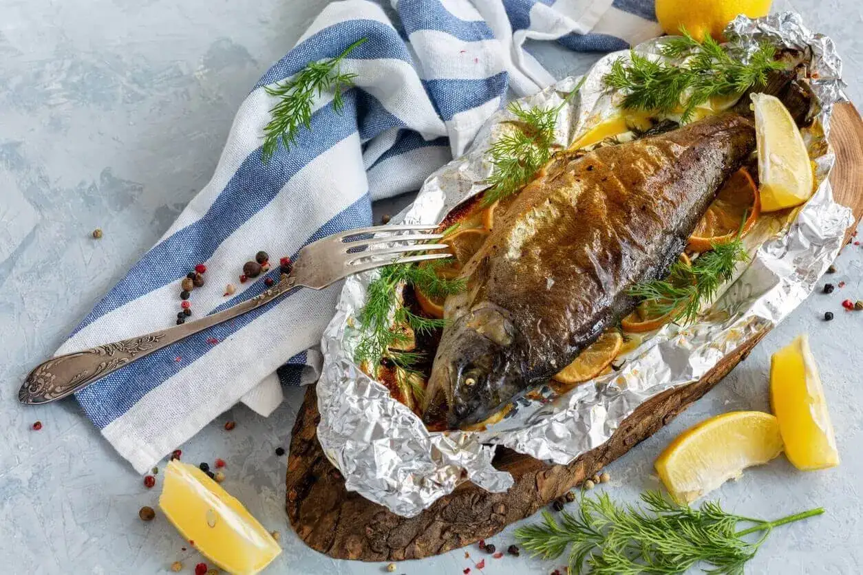 Złocisty filet z pstrąga z piekarnika, pieczony z cytryną i ziołami, podany na folii aluminiowej.